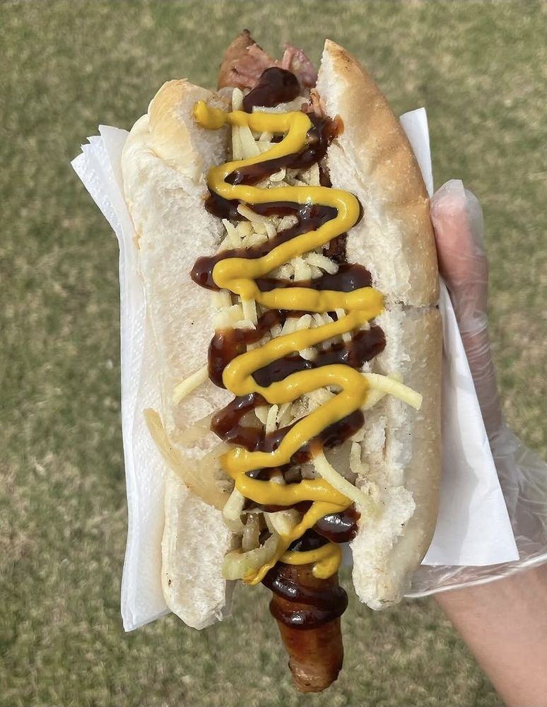 A sausage in a roll loaded with onion, cheese, mustard and barbecue sauce